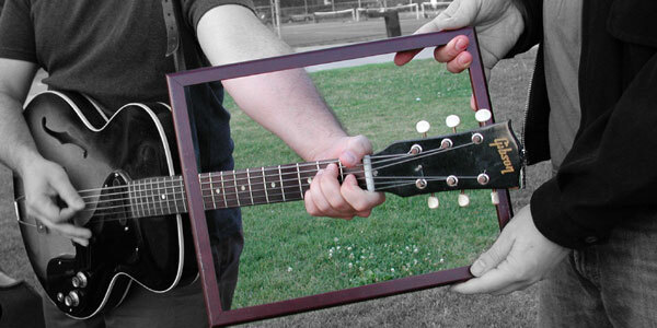 guitar player poking the neck of the guitar through a picture frame